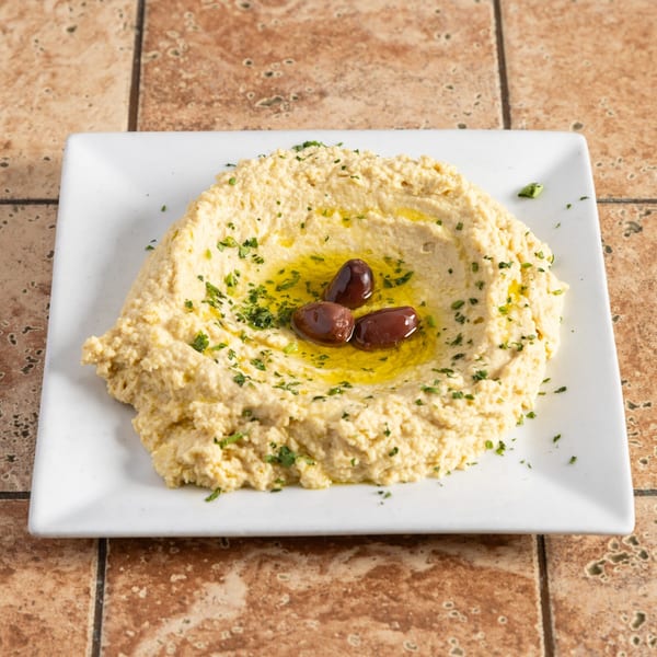 Creamy hummus with a drizzle of olive oil, fresh parsley, and three dark olives on a white plate.