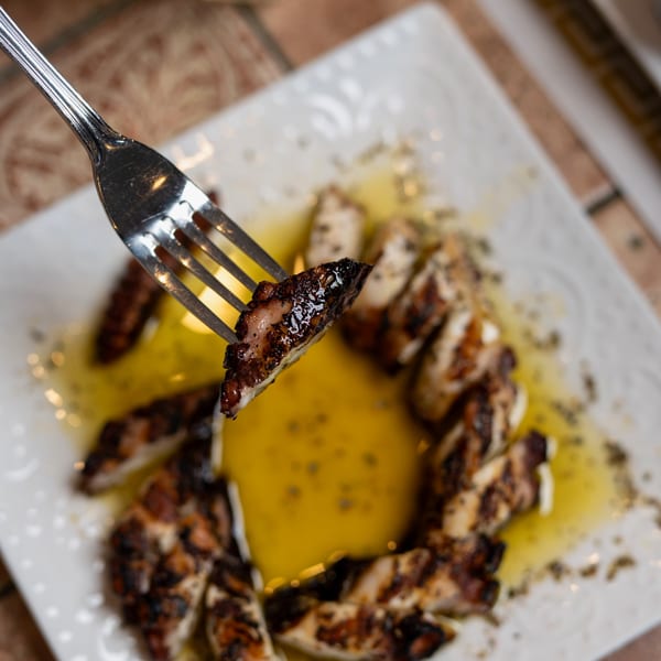 A fork lifts a piece of grilled calamari from a white plate with olive oil.