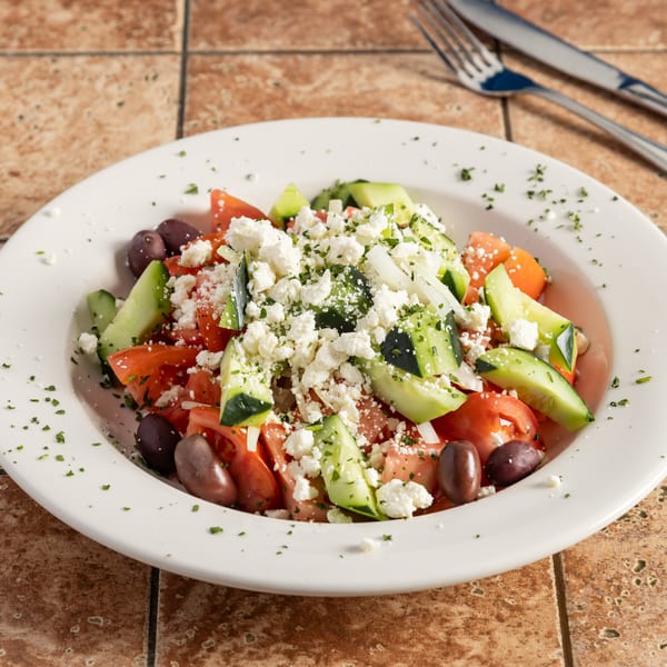 A vibrant Greek salad with tomatoes, cucumbers, olives, onions, and crumbled feta cheese.